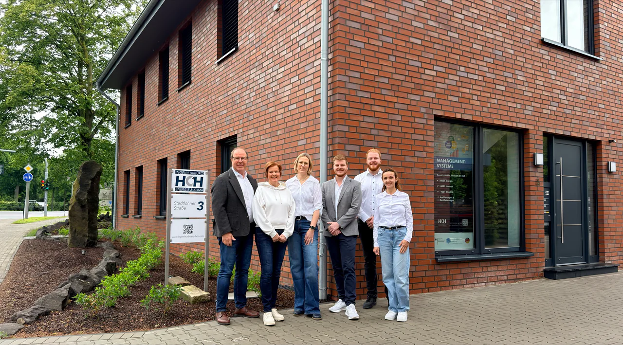 Team des HCH Ingenieurbüros vor dem Bürogebäude mit Vorgarten, Firmenschild, Roll-up zu Managementsystemen und Eingangstür
